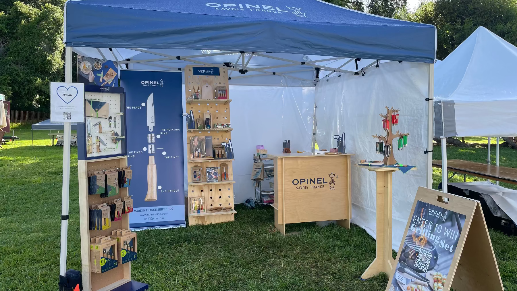 Opinel brand booth at an outdoor event with promotional materials and a blue canopy.
