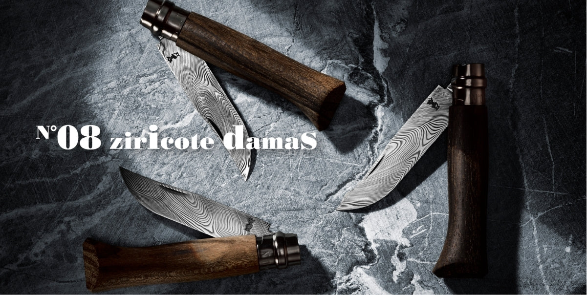 Four Damascus steel folding knives with dark wood handles are arranged on a dark gray stone background. White text on the left reads 'N°08 ziricote damaS'.